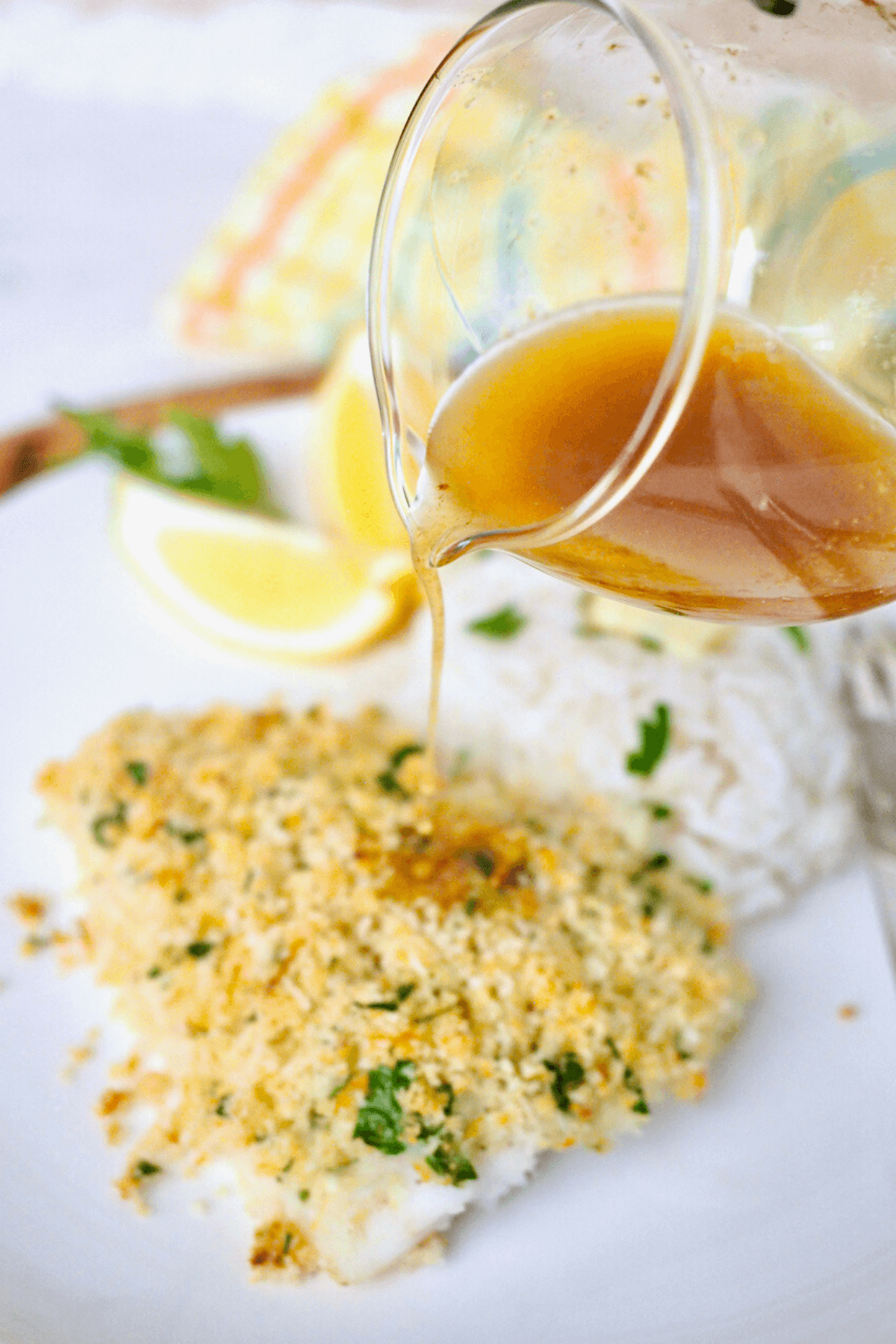 Pouring browned butter lemon garlic sauce over the top of the baked cod.