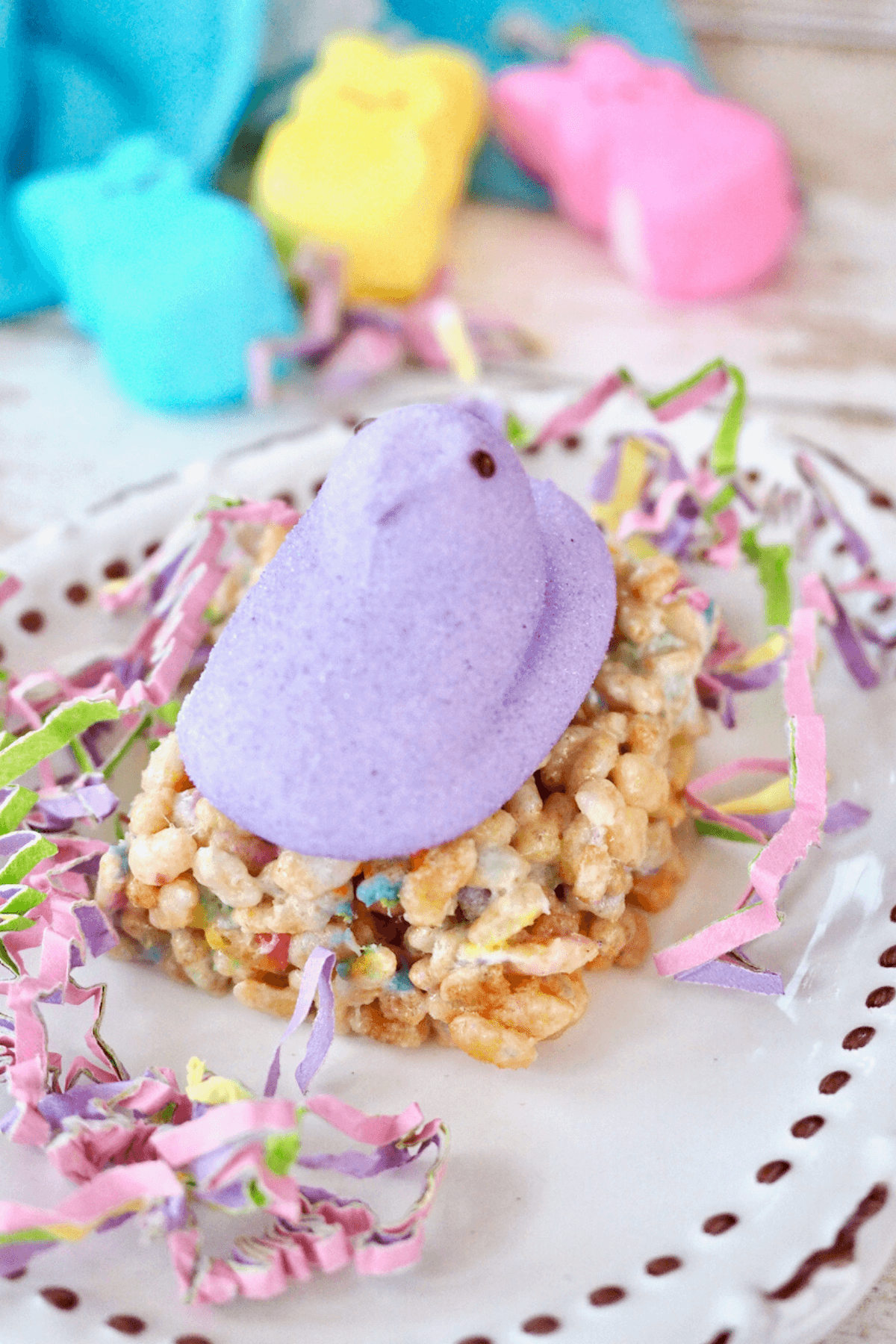 Purple Marshmallow Peep on top of Peep Rice Krispie Treat square on plate with confetti. 