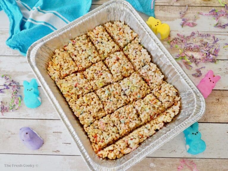 A large foil pan filled with cut, peeps rice krispie treats with Peeps marshmallow treats scattered around.