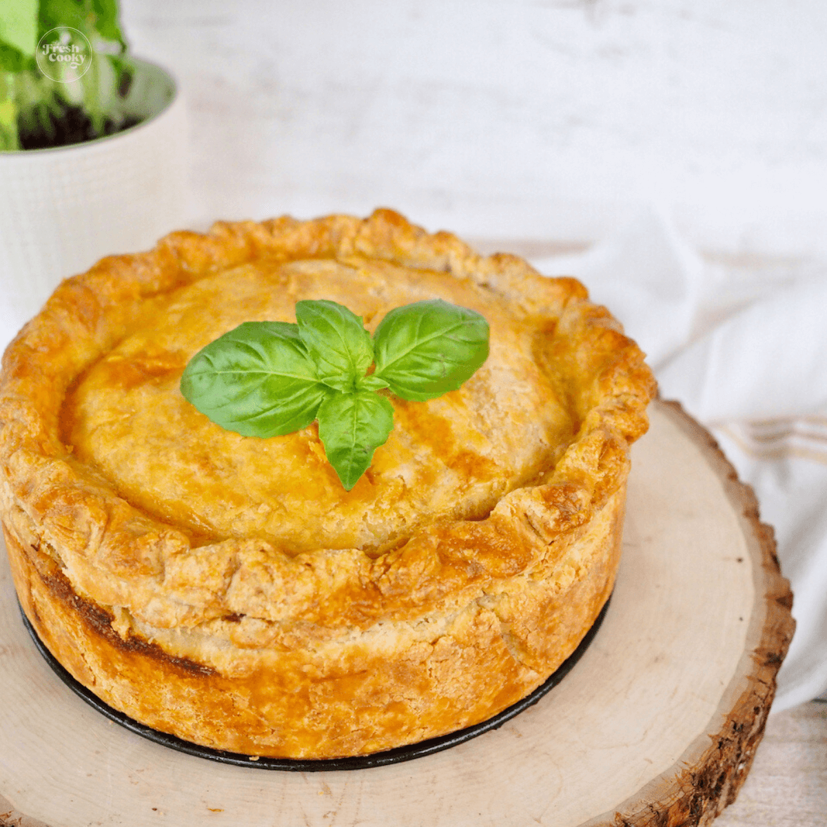 Square image of whole Pizza Rustica Easter Pie on a wooden tray garnished with fresh basil.