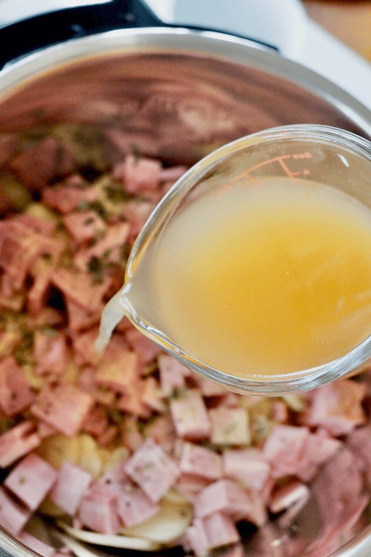 Pouring broth over the top of the potatoes and ham. 
