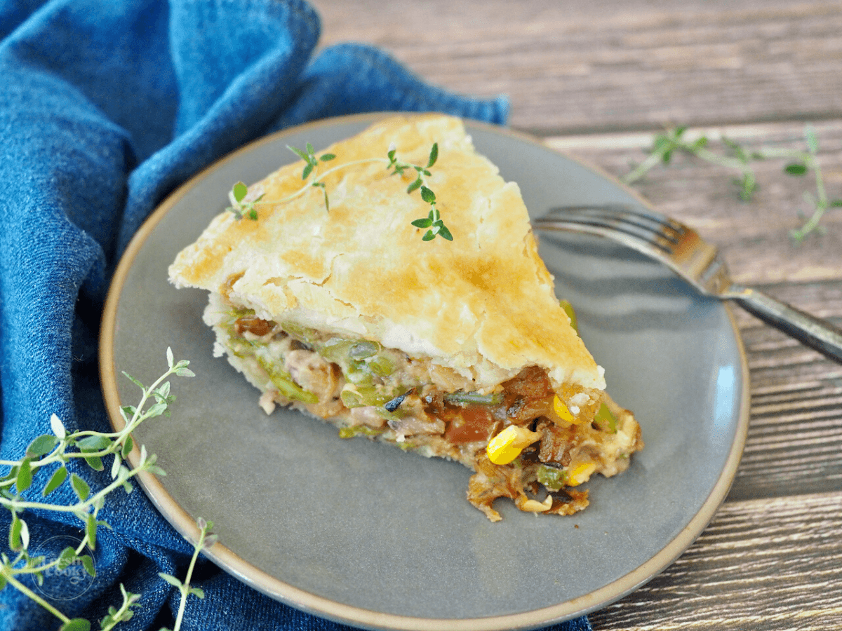 Slice of ham pot pie on plate with fork and fresh thyme garnish.