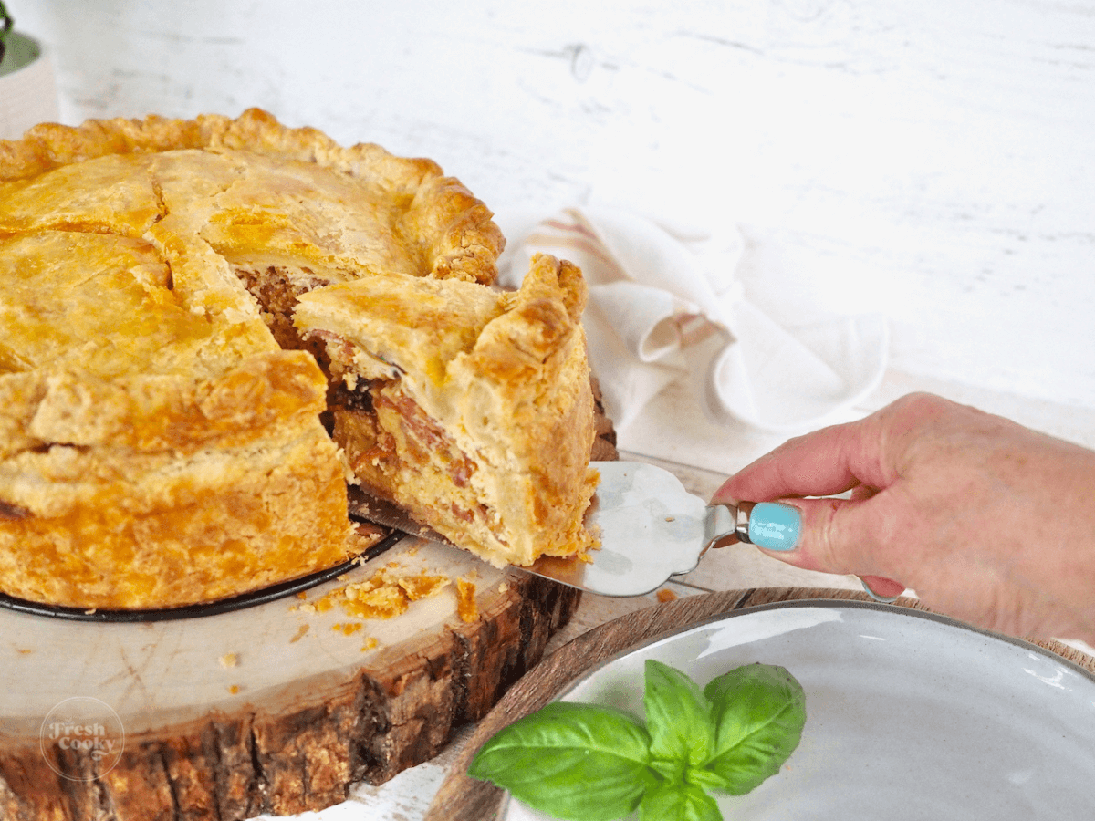 Hand pulling slice of pizza rustica out of the whole pie on pie server.