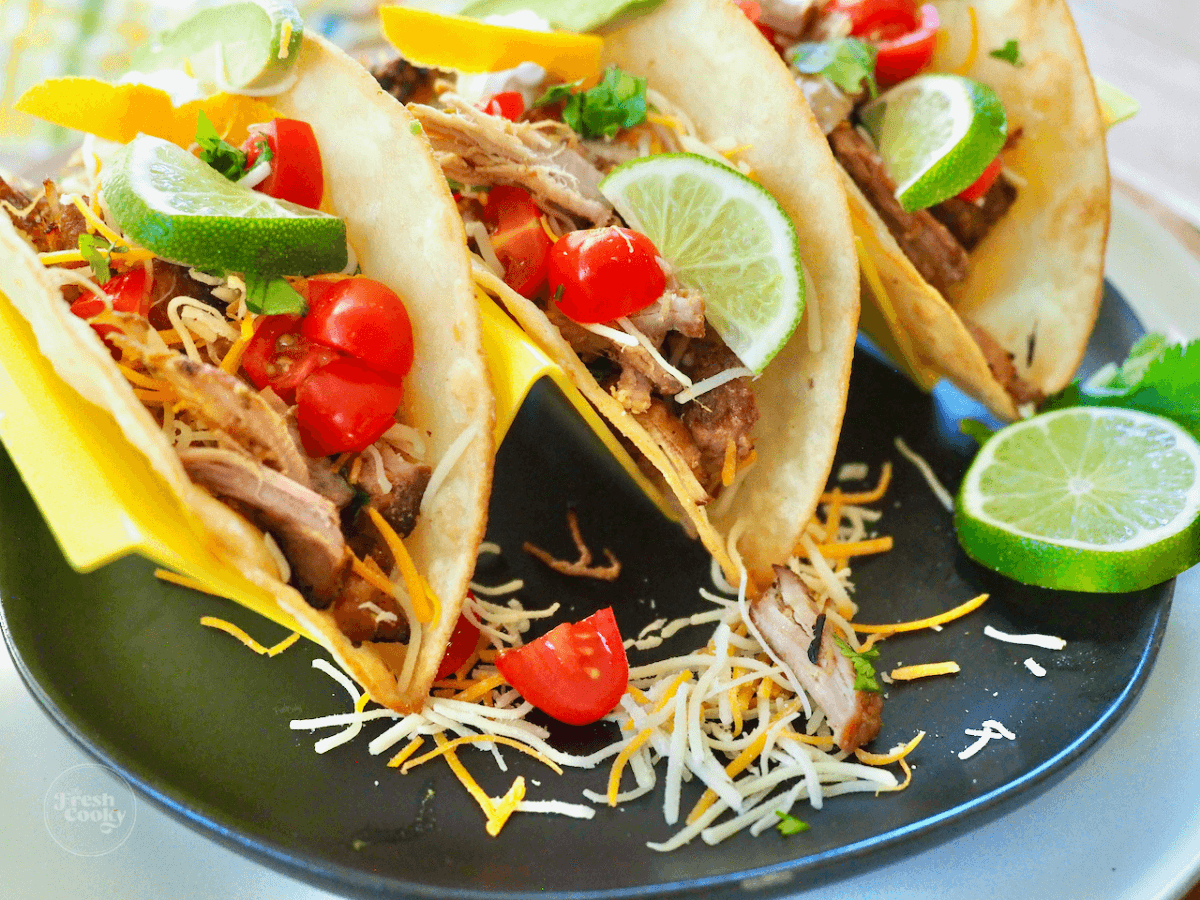 Instant Pot carnitas tacos on plate with tomatoes, avocado, cheese and toppings.
