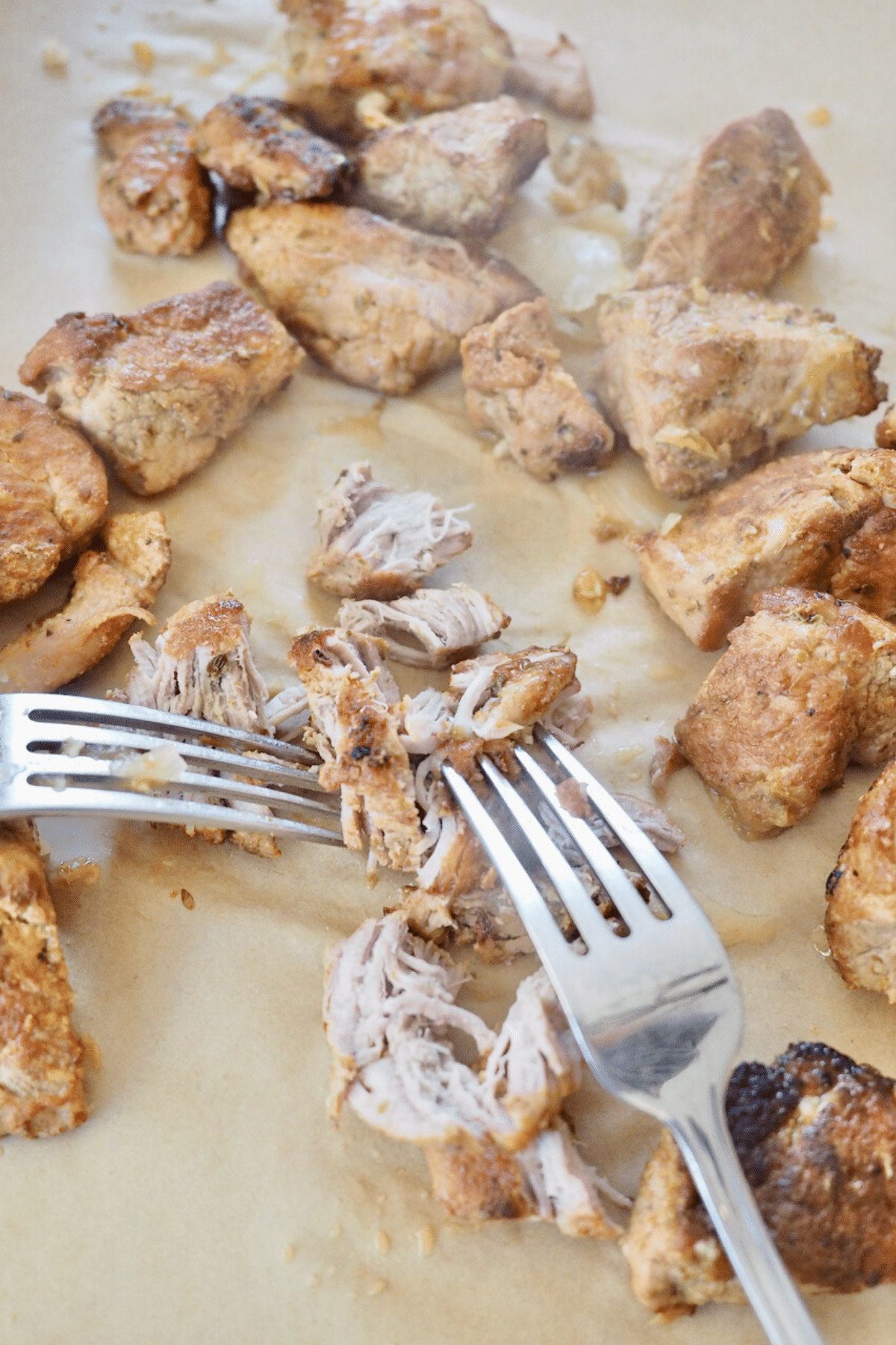 Shredding pork carnitas with two forks on sheet pan.