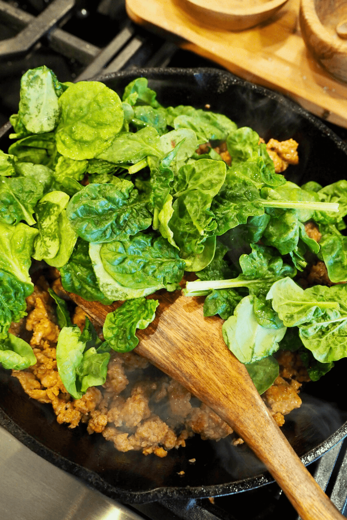 Adding fresh baby spinach to hot sausage mixture. 