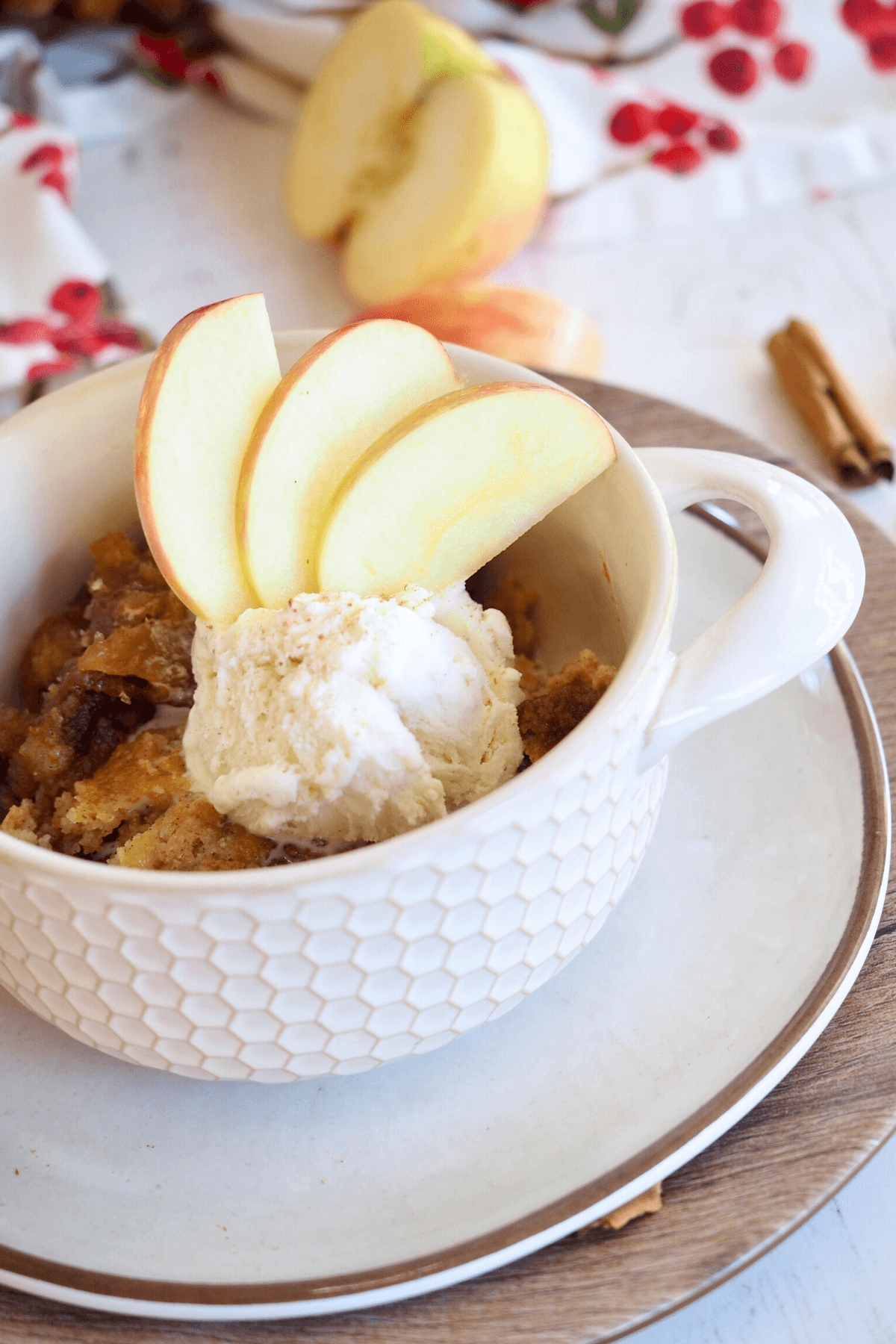 Caramel apple dump cake in pretty bowl topped with scoop of vanilla ice cream a sprinkle of cinnamon and three fresh sliced apples on top.