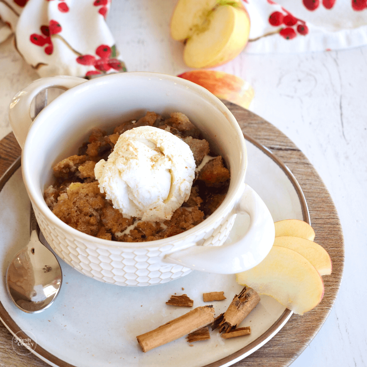 Caramel Apple Dump Cake Recipe in pretty bowl topped with ice cream with apples and cinnamon on the plate.