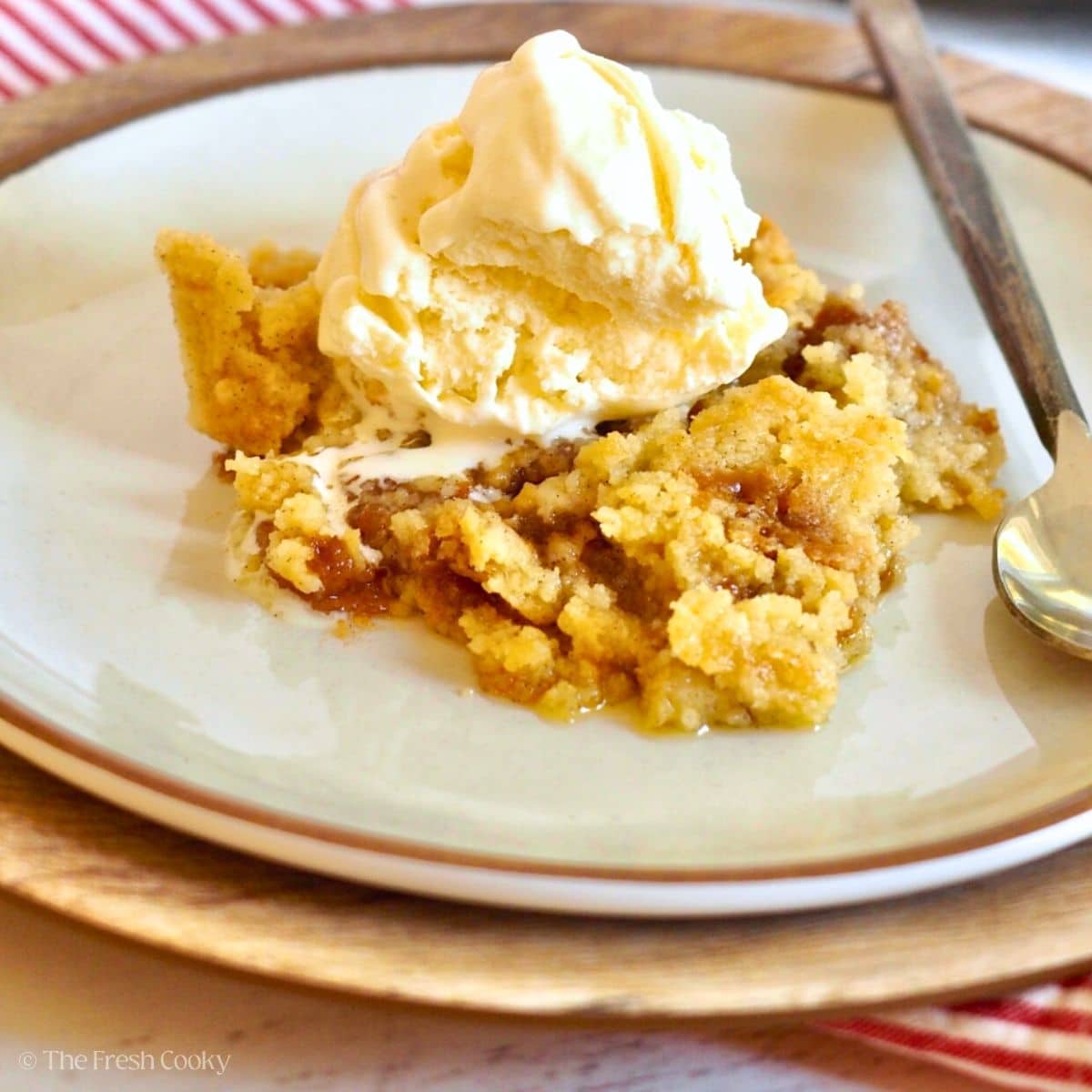 Serving of apple pie dump cake with caramel and topped with vanilla ice cream.