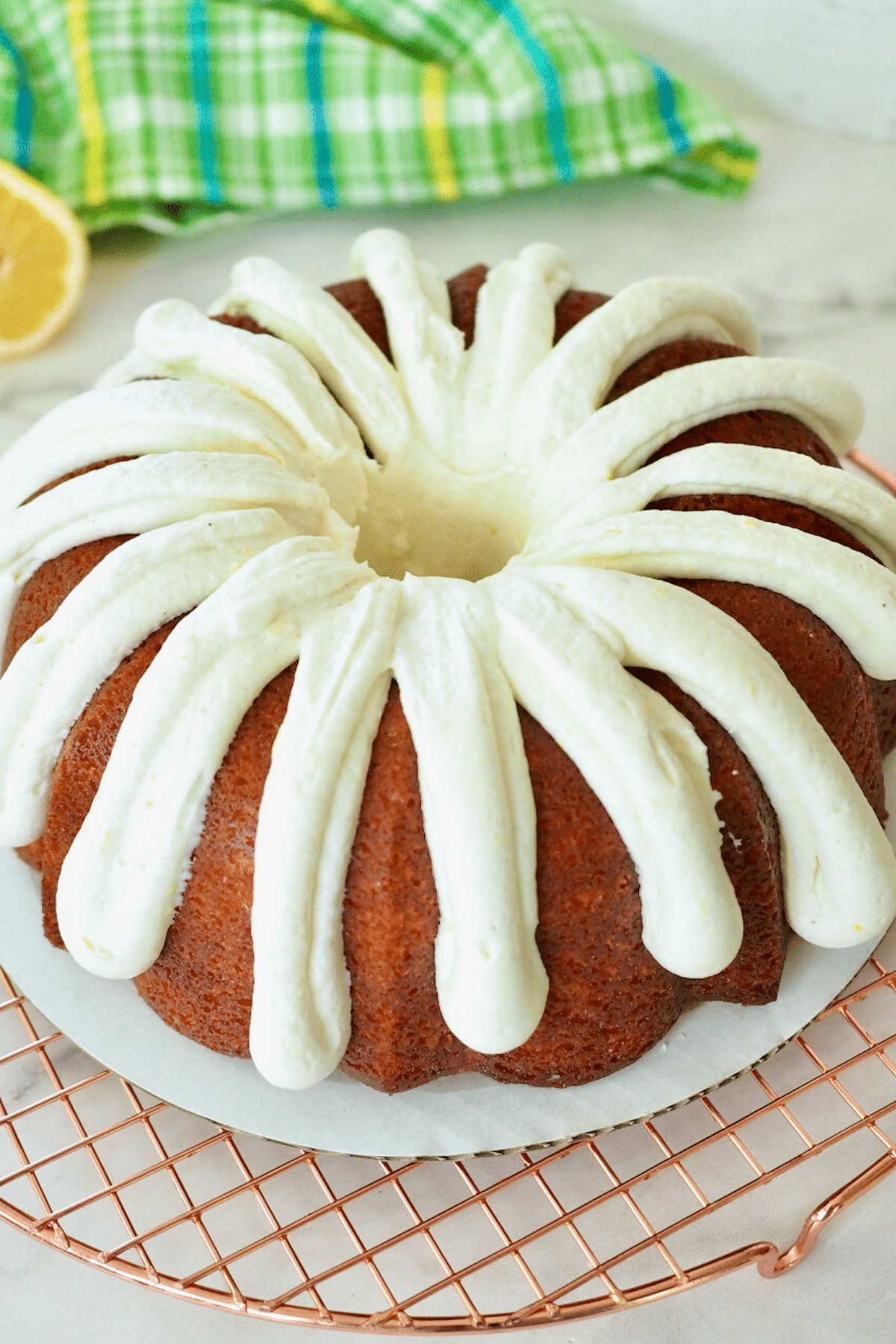 Lemon Bundt Cake with cream cheese frosting on cardboard on wire rack.