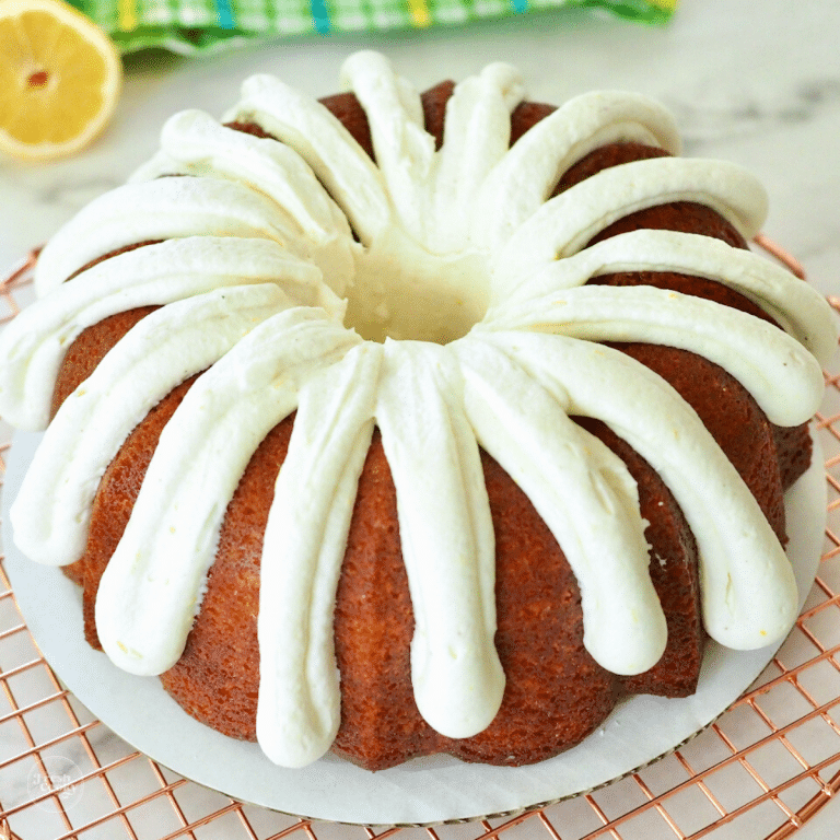 Lemon bundt cake on wire rack with fingers of cream cheese frosting with sliced lemon behind.