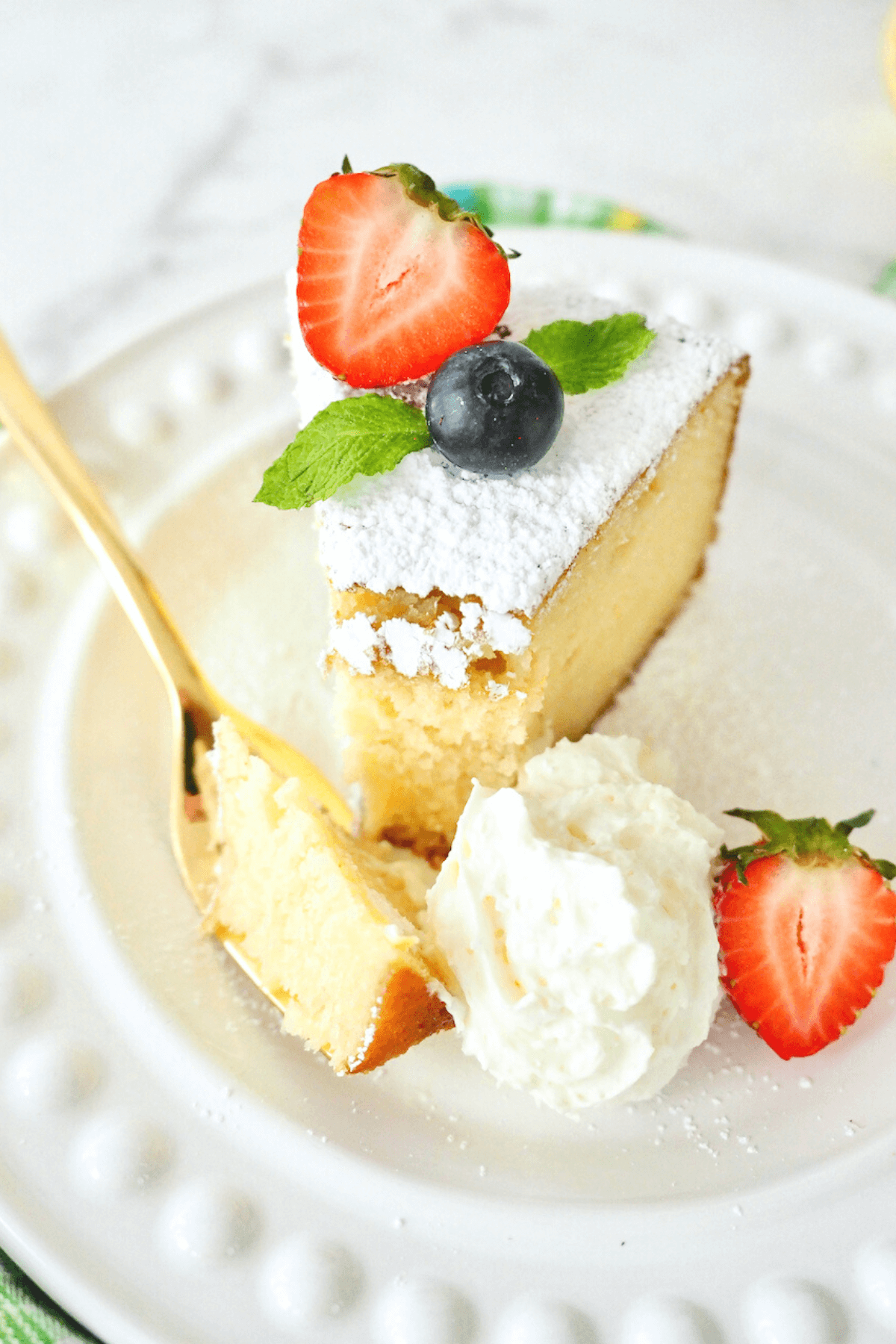 Lemon ricotta cake recipe with gold fork and bite on the fork, garnished with cream cheese and berries.