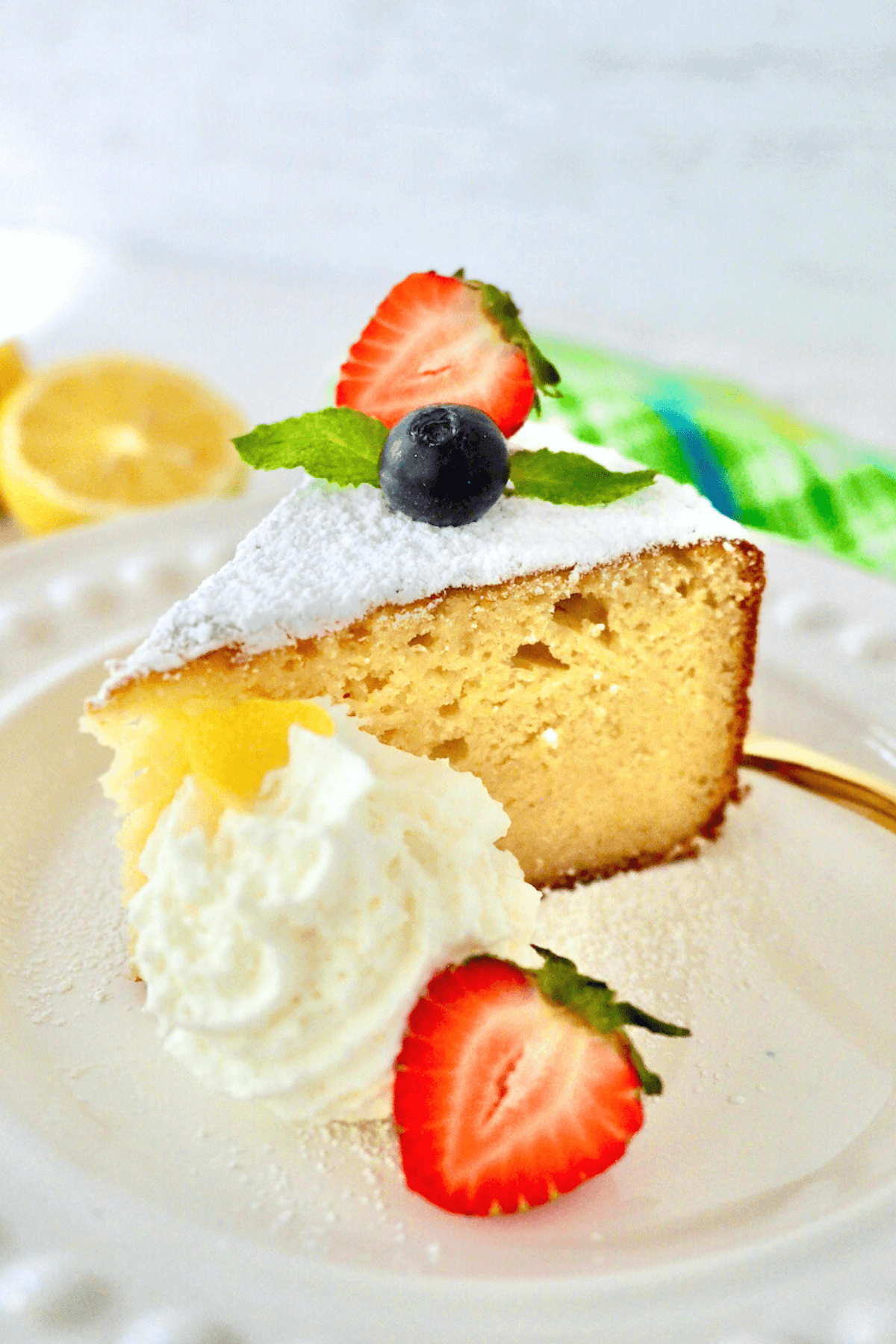 Lemon ricotta cake slice on plate with whipped cream and garnished with blueberries and strawberries.