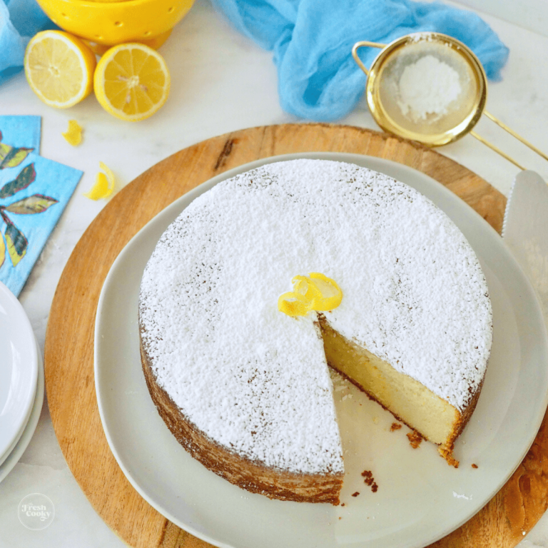 Lemon Ricotta Cake Recipe with image of cake on platter with slice removed, topped with powdered sugar and lemon rind.