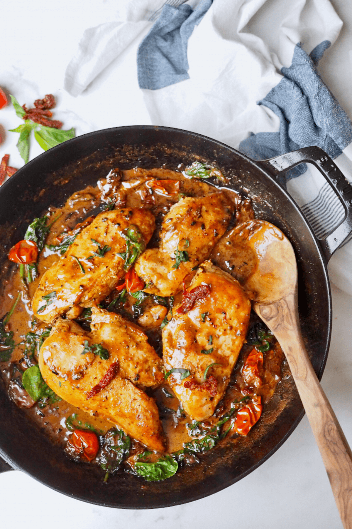 One pan creamy tuscan chicken in skillet with wooden spoon.