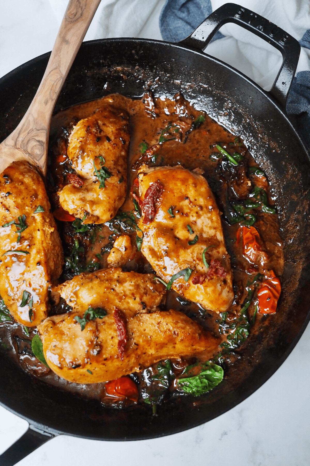 One pan chicken with creamy Tuscan sauce in Staub everyday pan with wooden spoon.