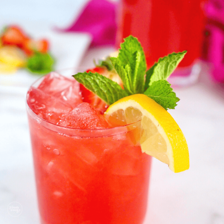 Pink lemonade vodka punch cocktail in a glass with a lemon wedge, mint and a slice of strawberry.