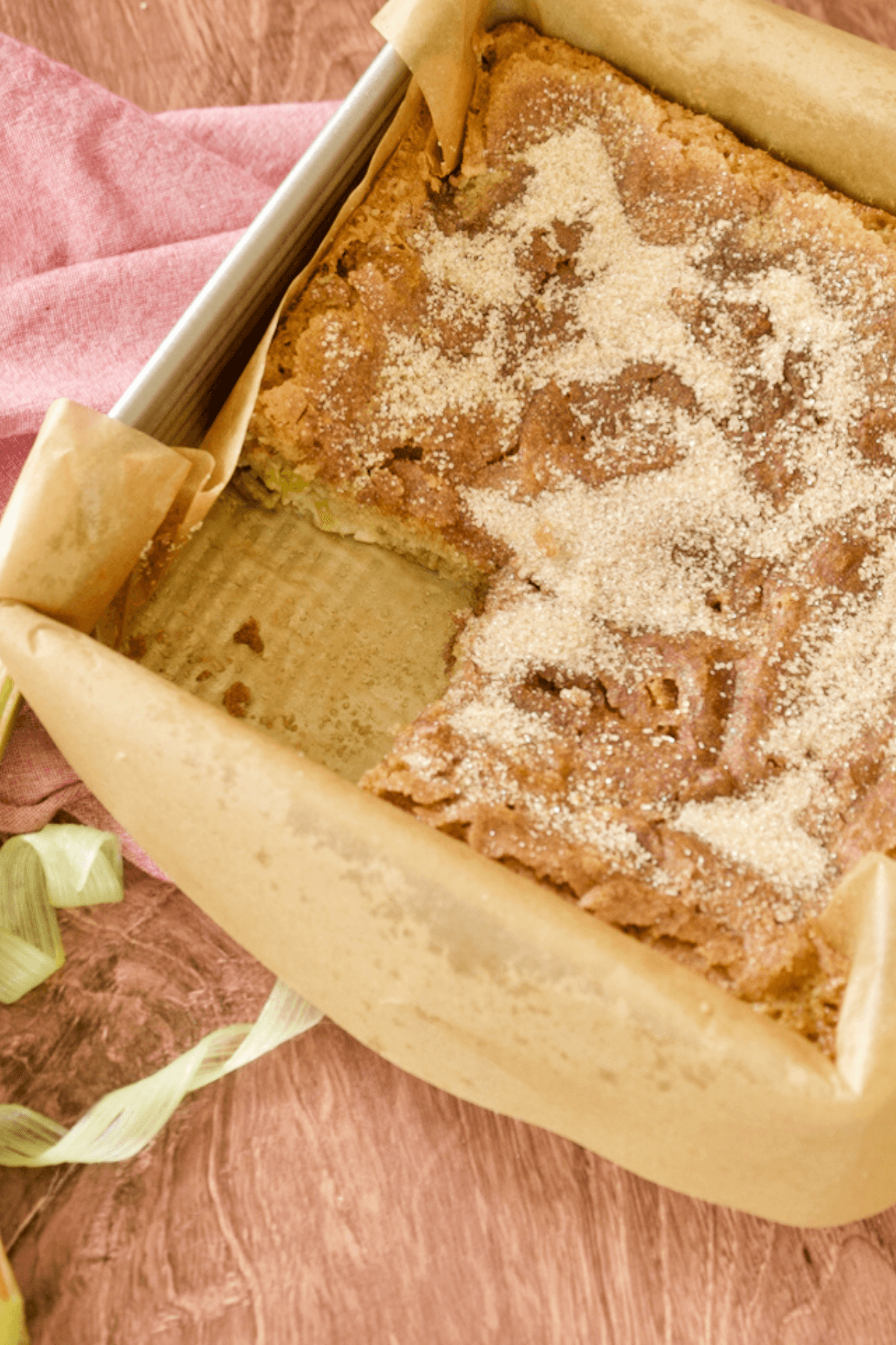 Image of 8x8 pan filled with baked rhubarb coffee cake with one slice removed and ribbons of rhubarb nearby.