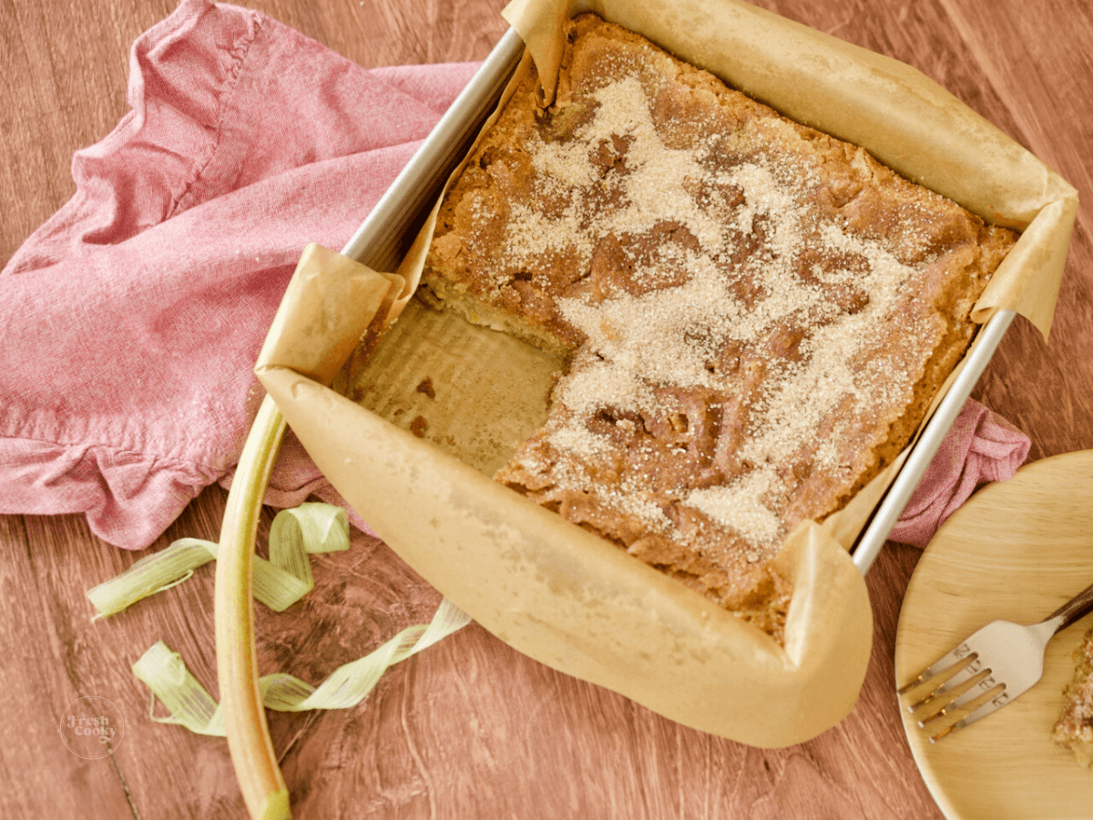 Rhubarb Coffee Cake in pan with slice removed and ribbons of rhubarb laying nearby.