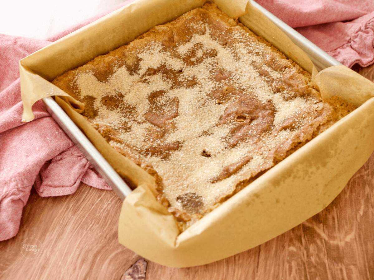 Pan of rhubarb coffee cake recipe on wood table with pink napkin behind.