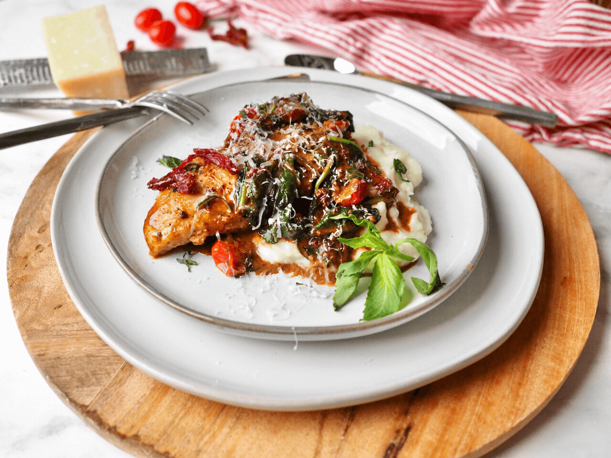 Creamy Tuscan Chicken over mashed potatoes with a sprig of basil.