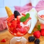 Strawberry shortcake wedge in a bowl loaded with juicy sliced strawberries and topped with whipped cream and a sprig of mint.