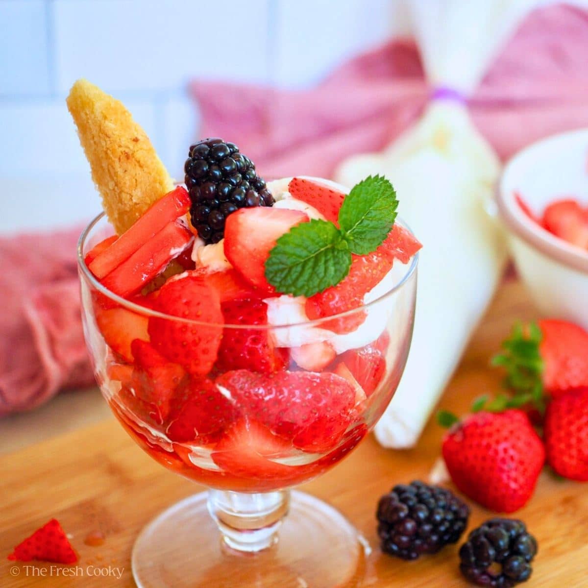 Strawberry shortcake wedge in a bowl loaded with juicy sliced strawberries and topped with whipped cream and a sprig of mint.