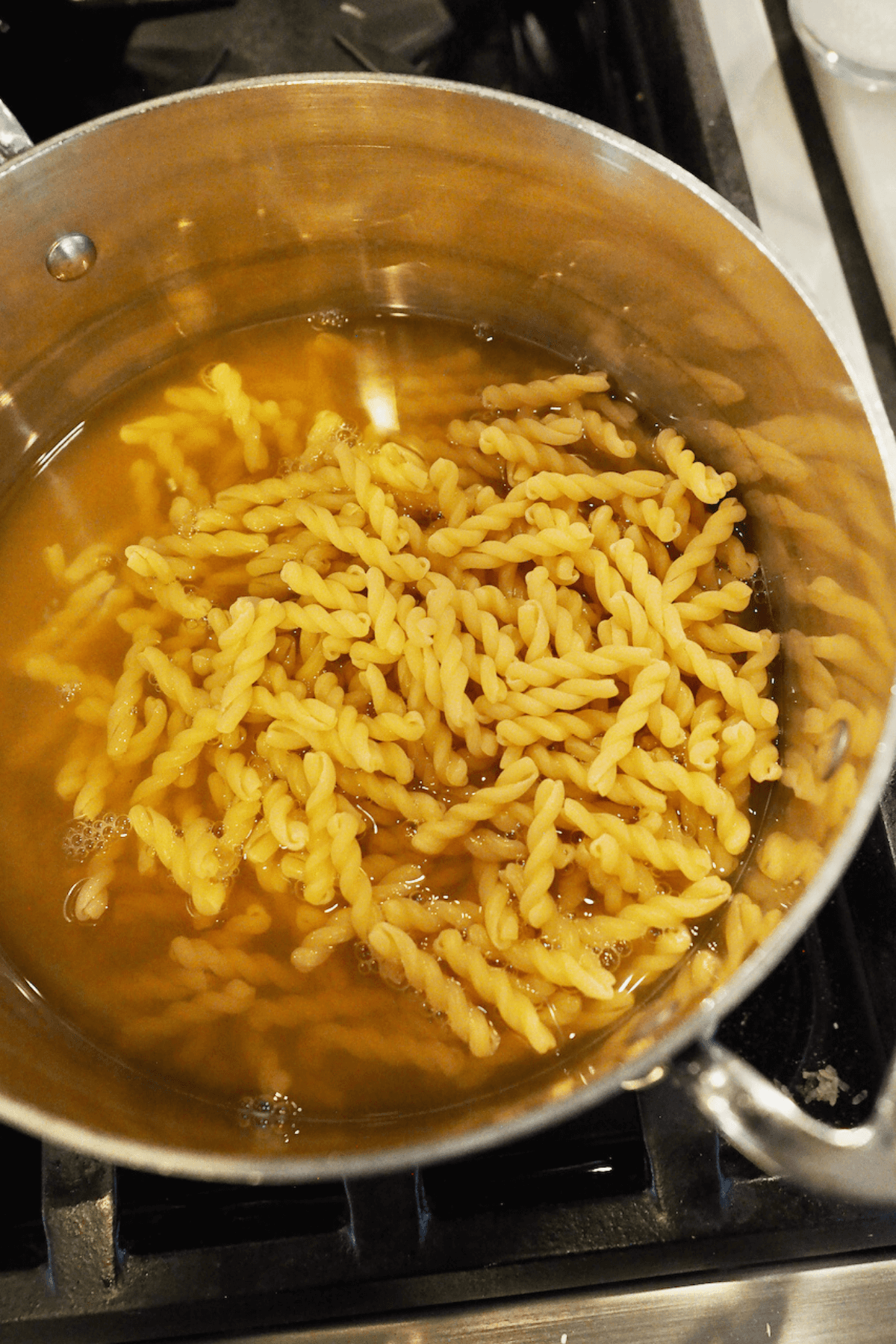 Adding chicken broth and gemelli pasta to pot. 