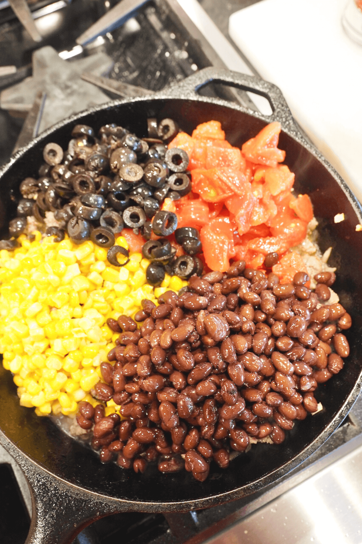 Adding black beans, corn, tomatoes and sliced olives into meat mixture. 
