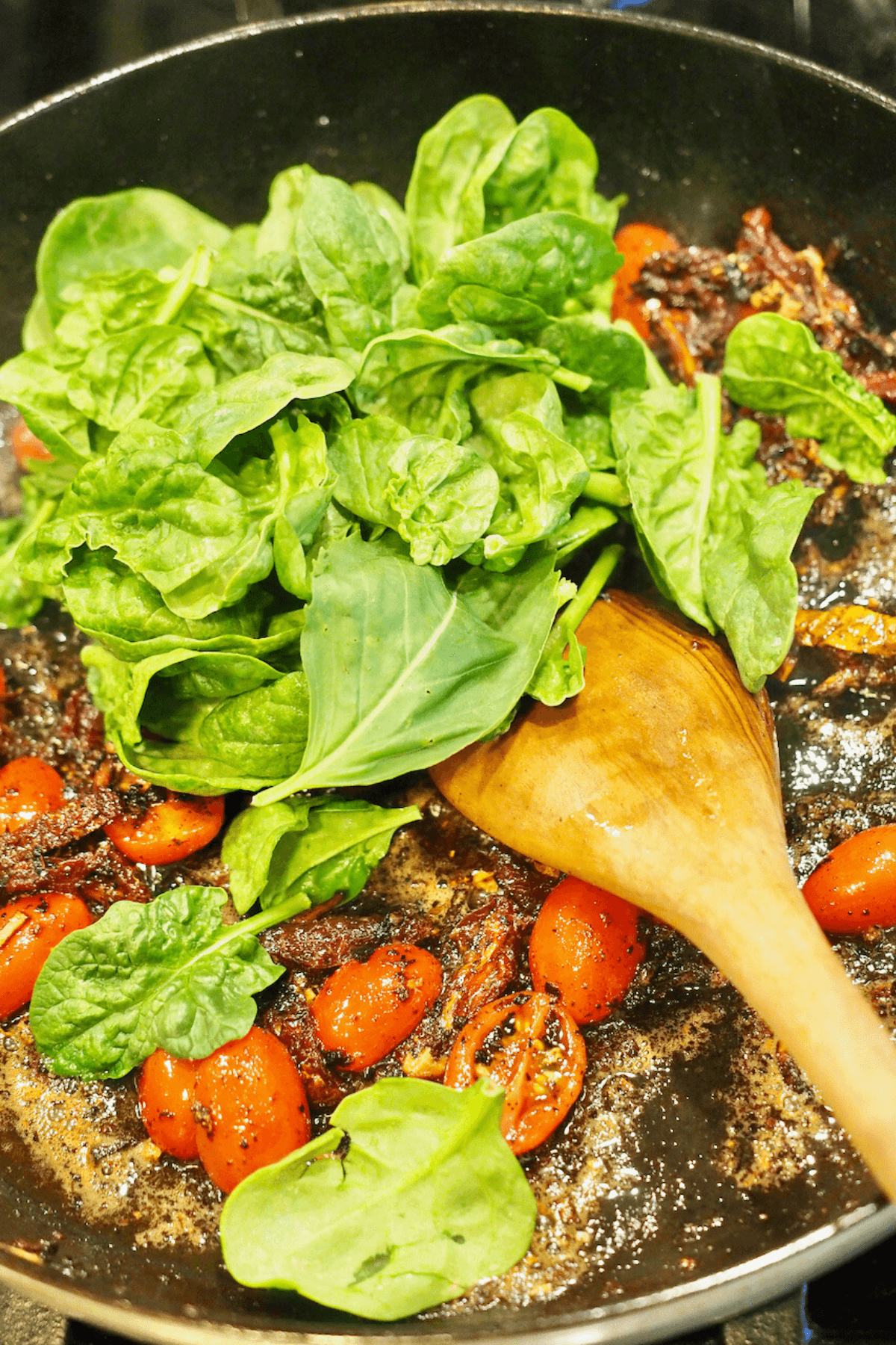 Adding baby spinach to pan to wilt. 