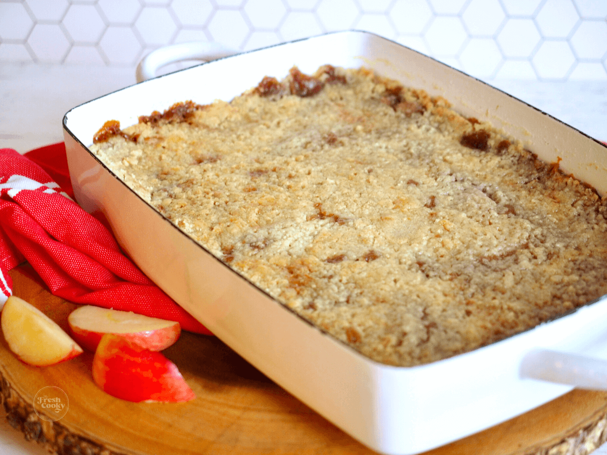 Pan of caramel apple dump cake on board with sliced apples nearby.