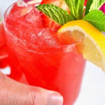 Hand holding a pink lemonade vodka cocktail.