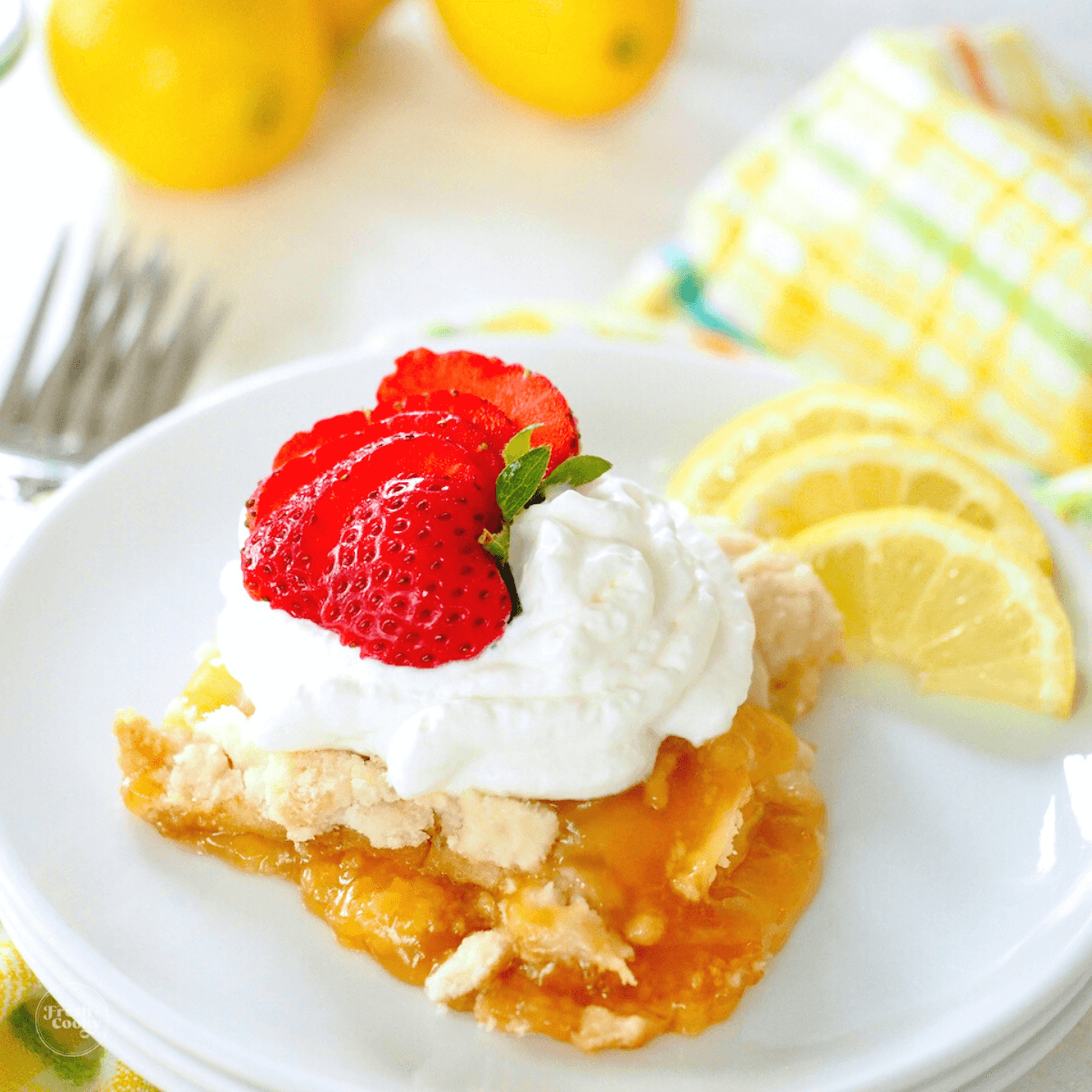 Lemon dump cake serving on plate with whipped cream and sliced strawberry.