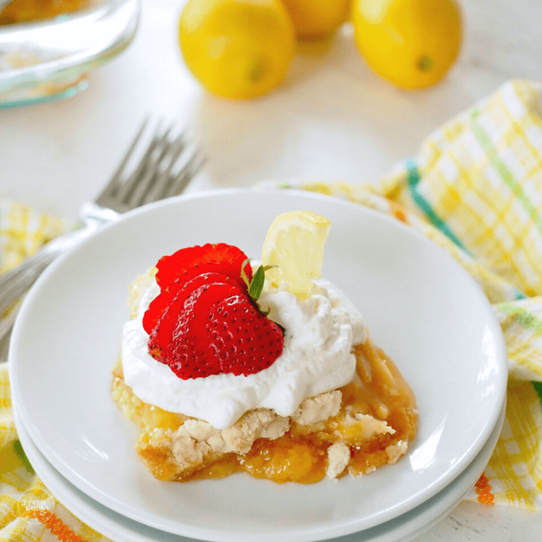 Lemon dump cake recipe on plate with forks behind, cake decorated with whipped cream and strawberries.