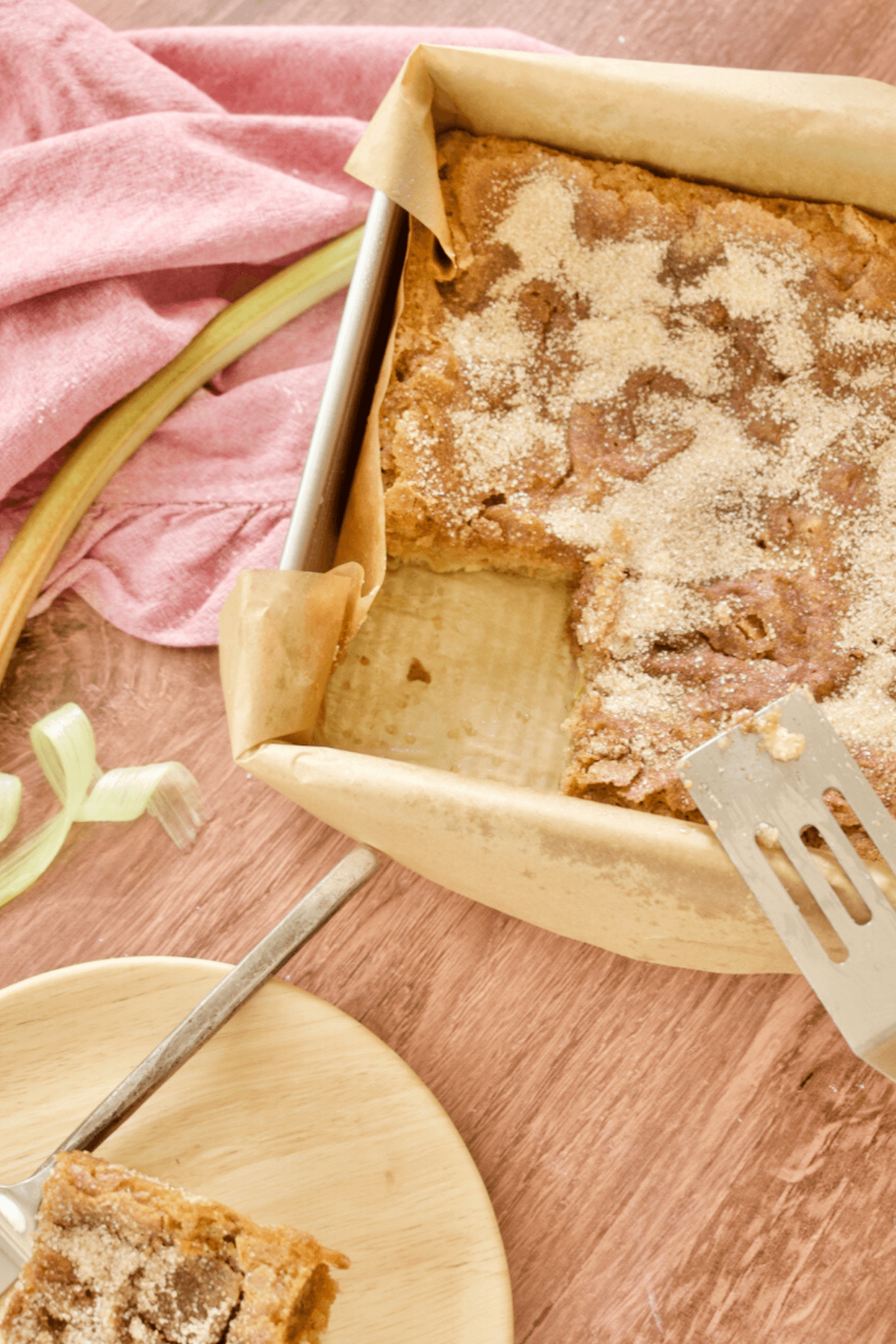 Slice removed from square pan filled with rhubarb coffee cake and plate with slice nearby.