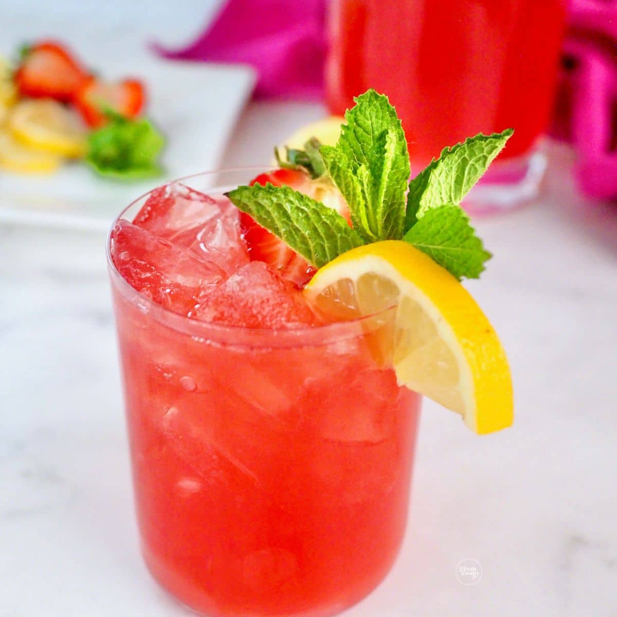Pink lemonade vodka cocktail garnished with mint, lemon and a strawberry.