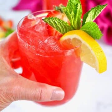 Hand holding a pink lemonade vodka cocktail.