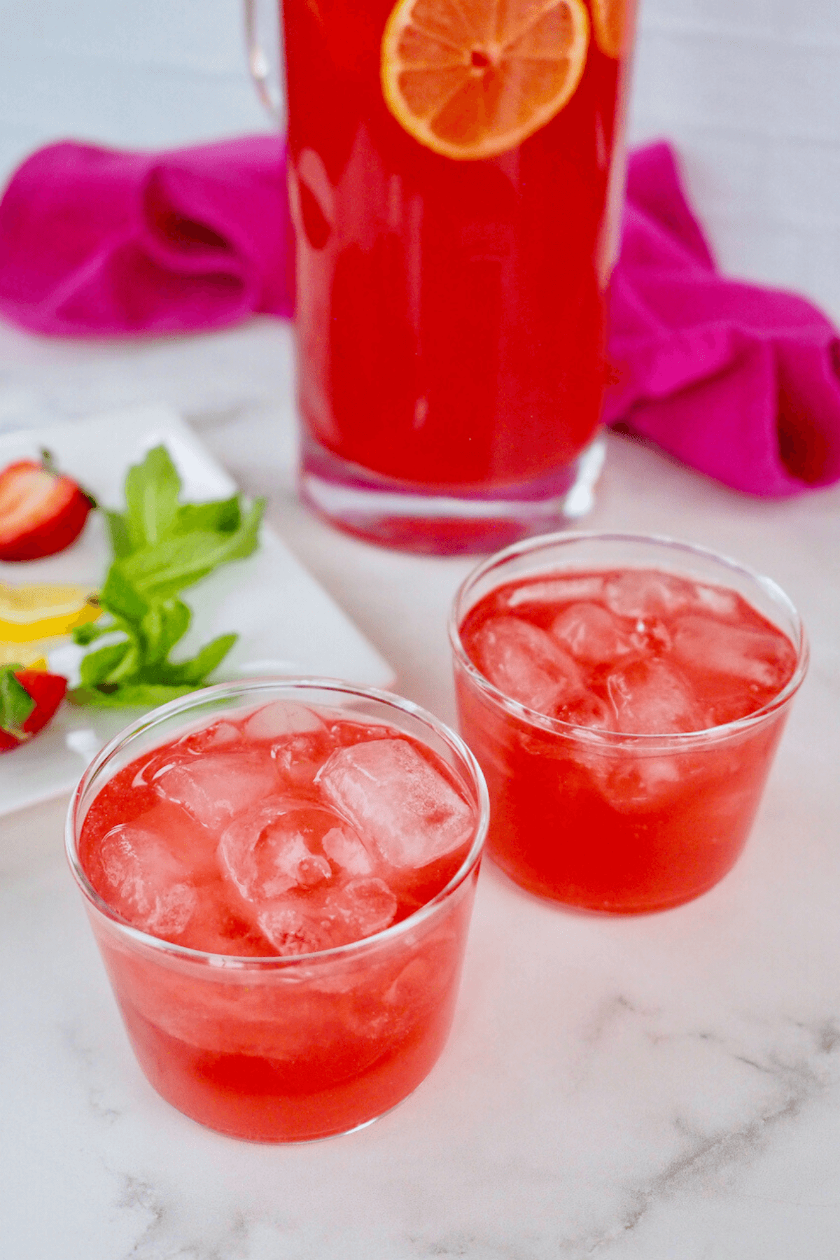Pink lemonade in small bodega glasses with pitcher of lemonade behind.