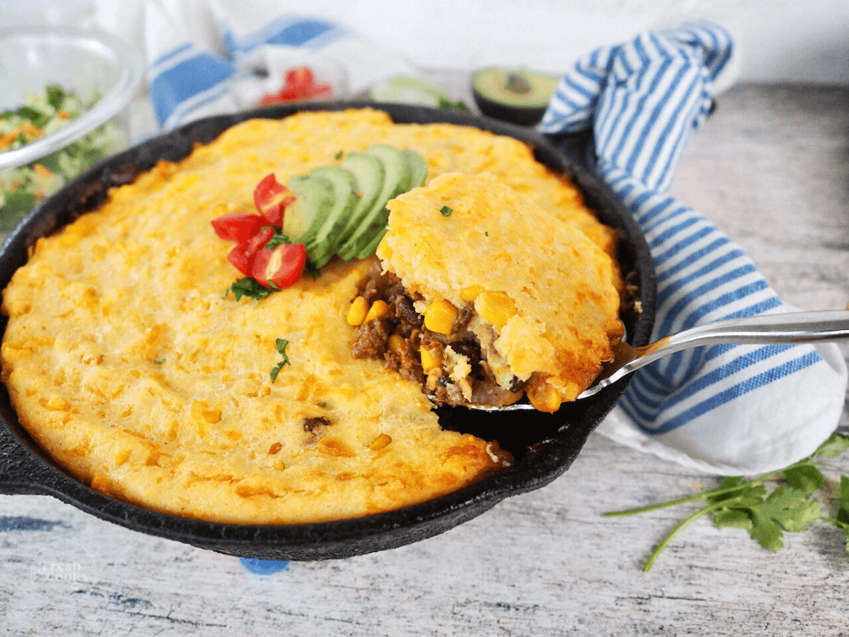 Hand scooping tamale pie recipe from skillet.