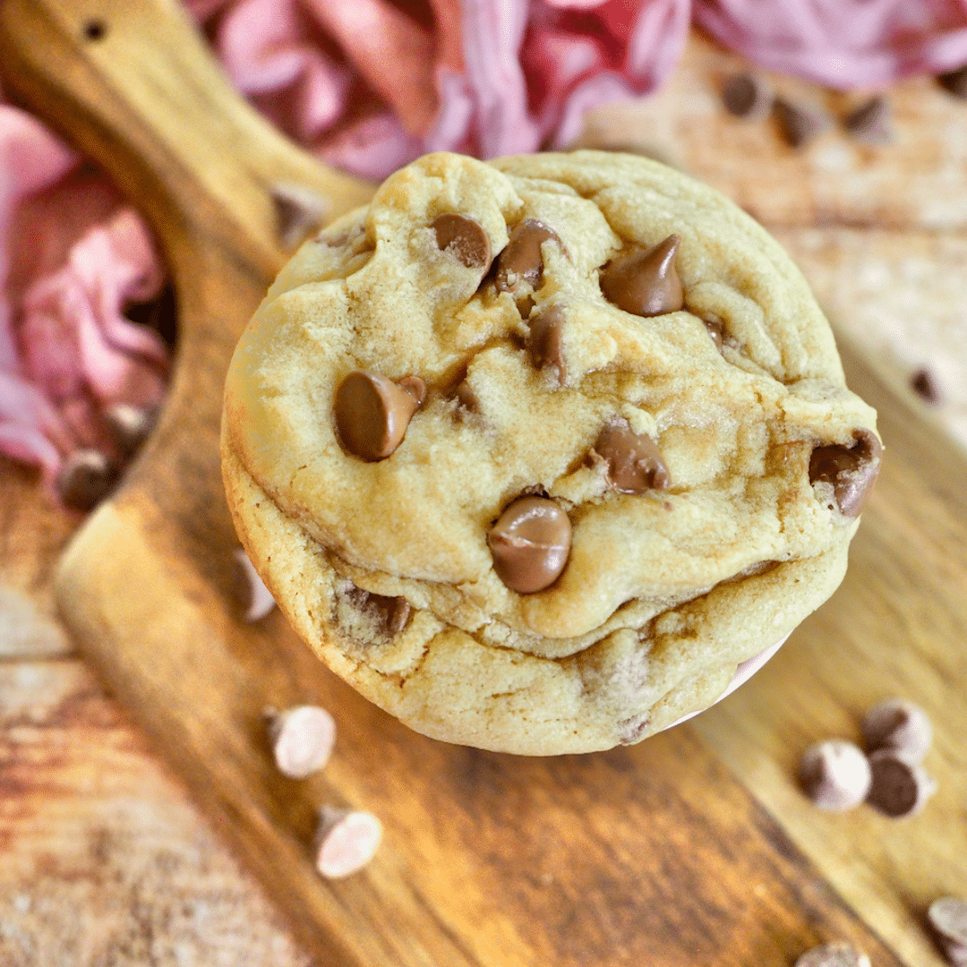 Crumbl Chocolate Chip Cookie Recipe with giant cookie on cutting board with milk chocolate chips surrounding.