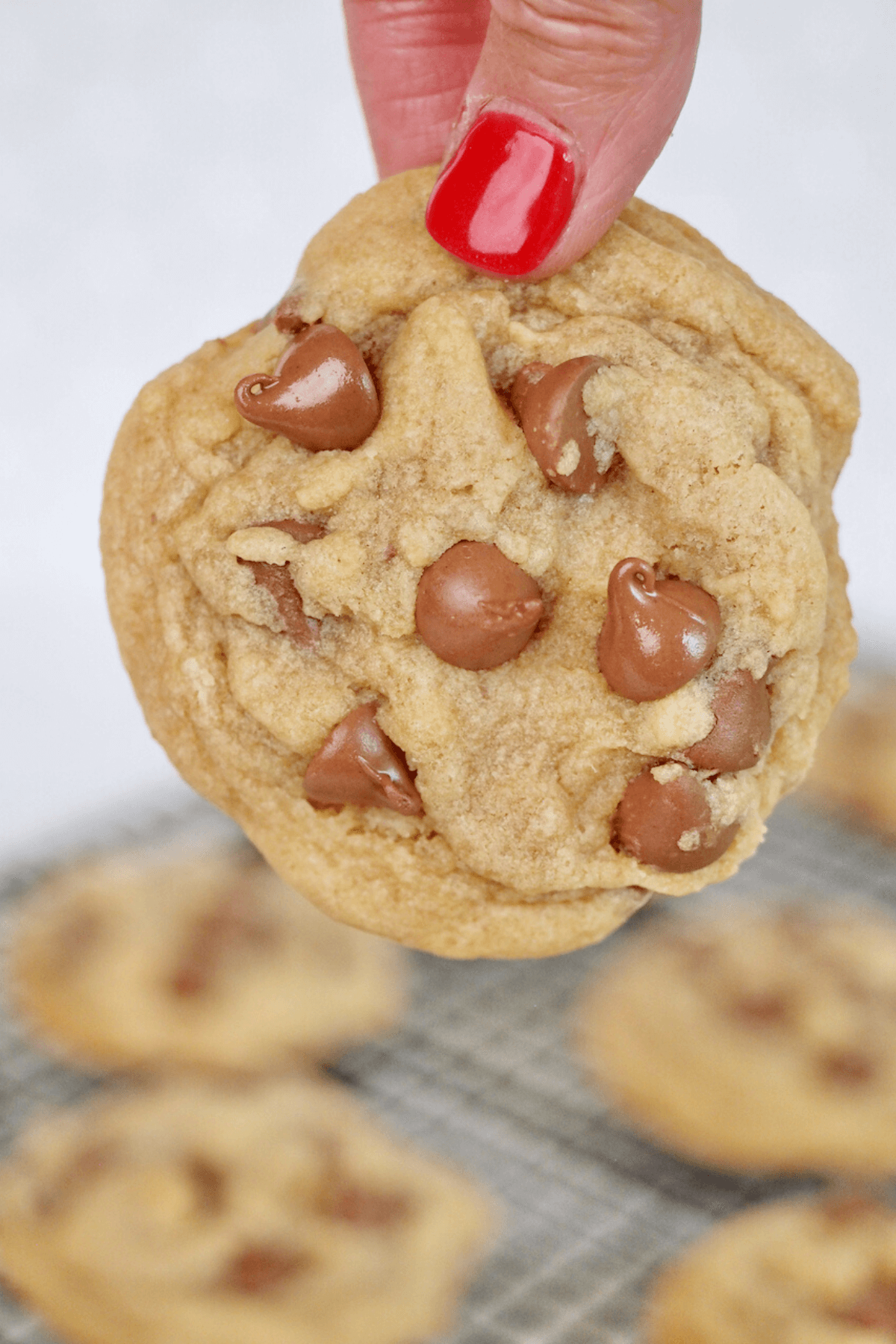 Hand holding giant copycat crumbl cookie with more cookies on cooling rack in background.