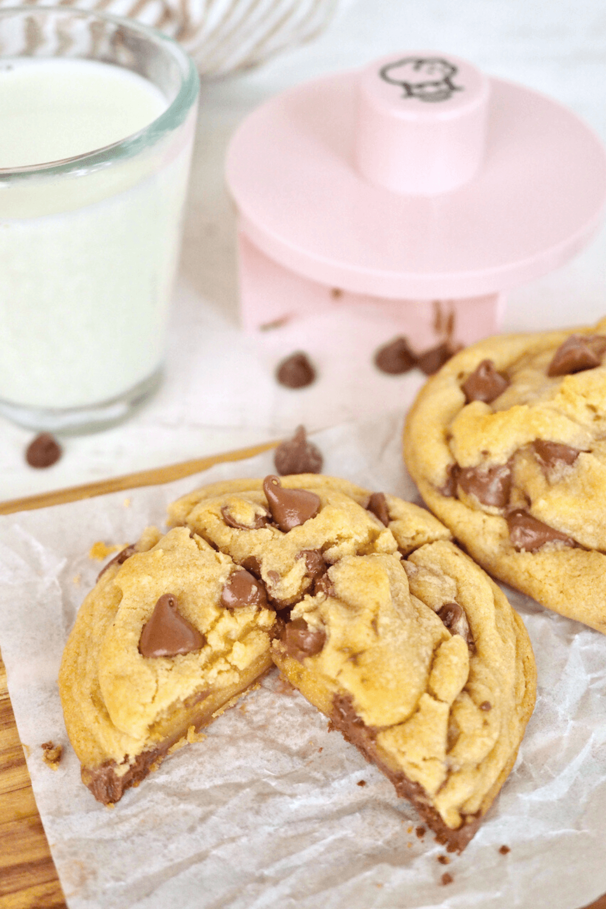 Giant copycat crumbl chocolate chip cookie cut into quarters on parchment with glass of milk and crumbl cookie cutter in background.