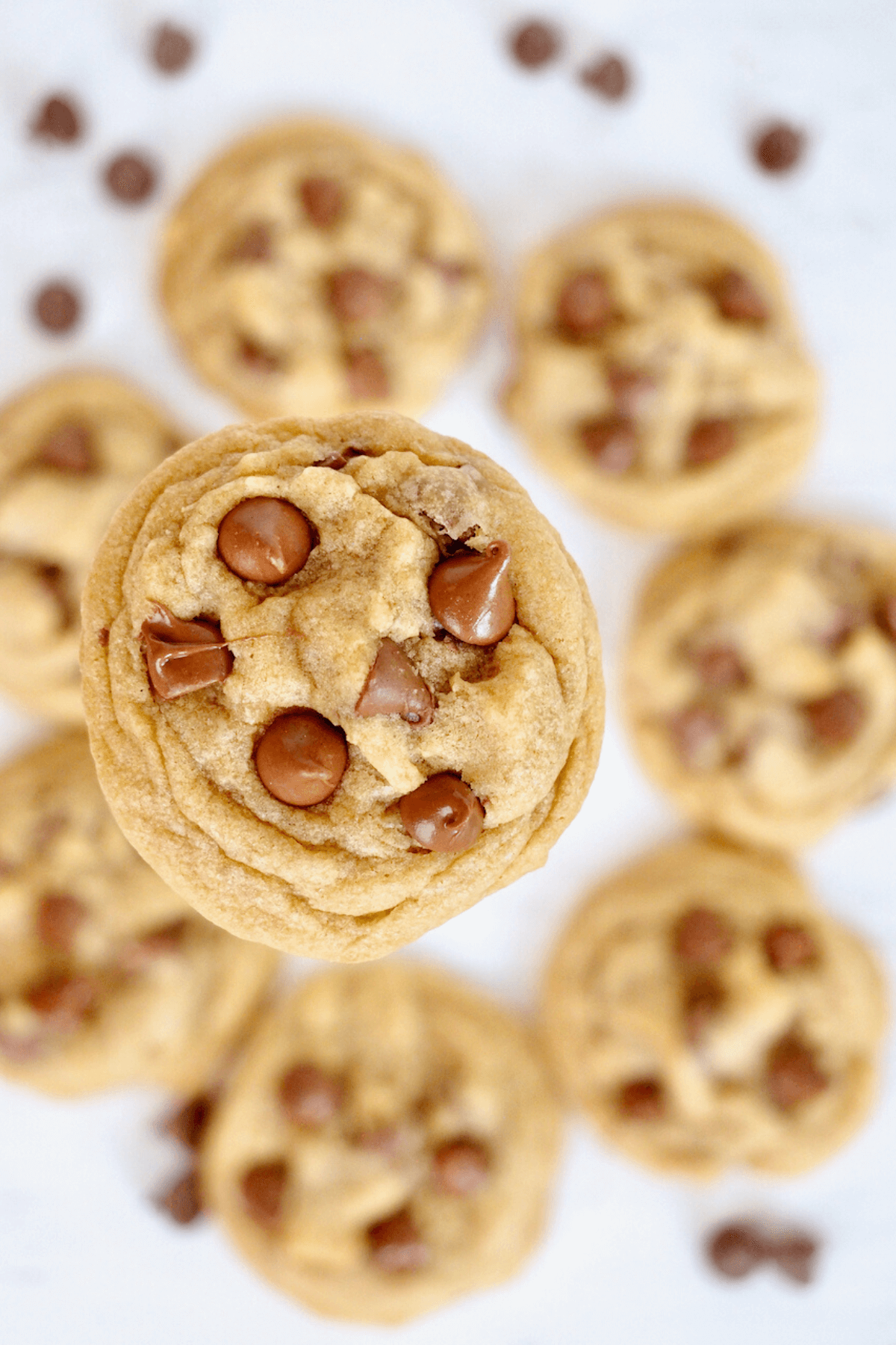 Regular Crumbl chocolate chip cookies with one in focus and the ones under surrounding that mini cookie.