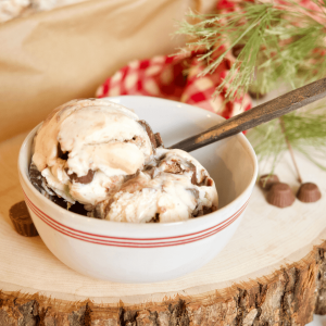 Moose tracks ice cream recipe in rustic bowl on wood slice with rustic spoon and checkered red and white napkin in background.