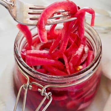 Fork pulling out pickled red onions from canning jar.