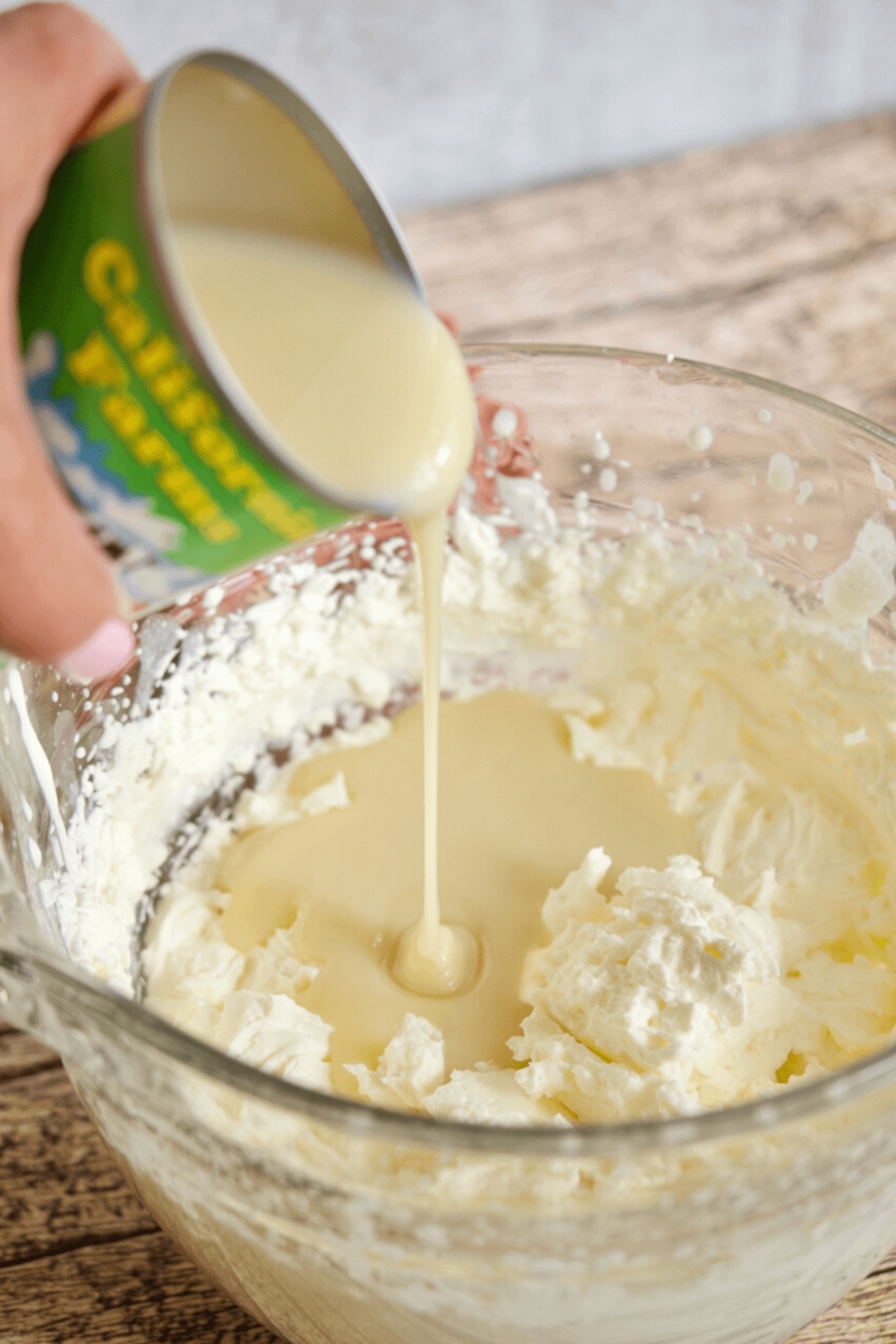 Hand pouring in can of organic sweetened condensed milk into whipped cream mixture.