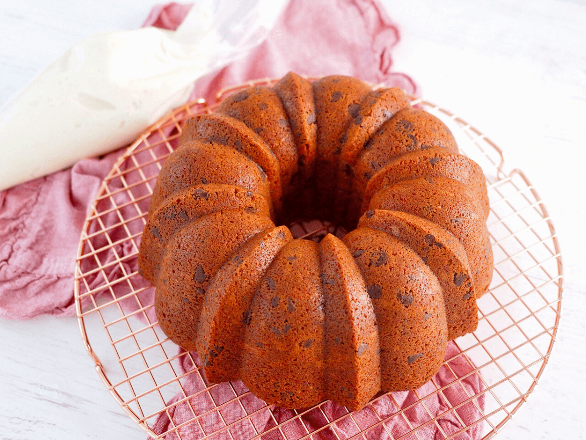 Red Velvet Bundt Cake unfrosted on cooling rack with frosting in piping bag behind.