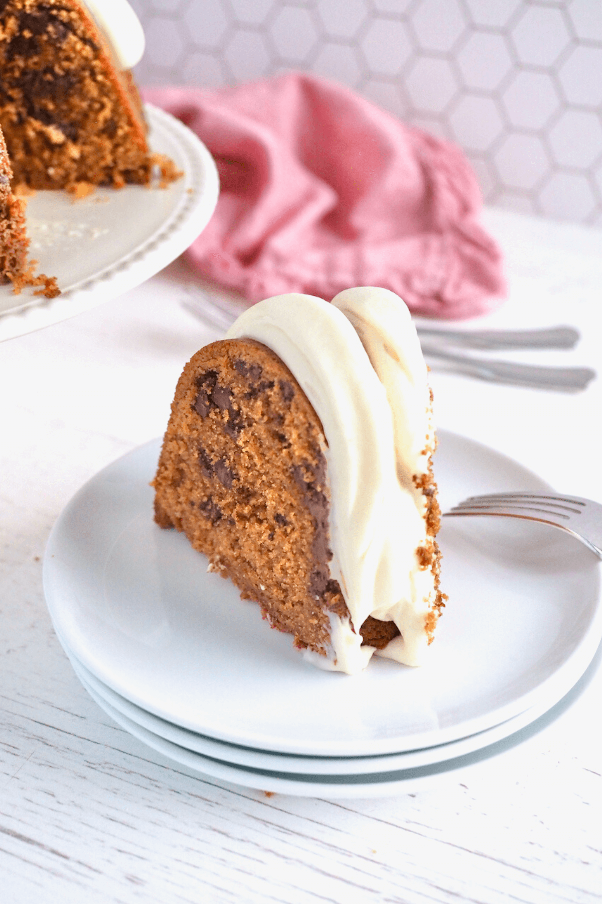 Slice of red velvet cake on a plate with the bundt on a cake stand behind.