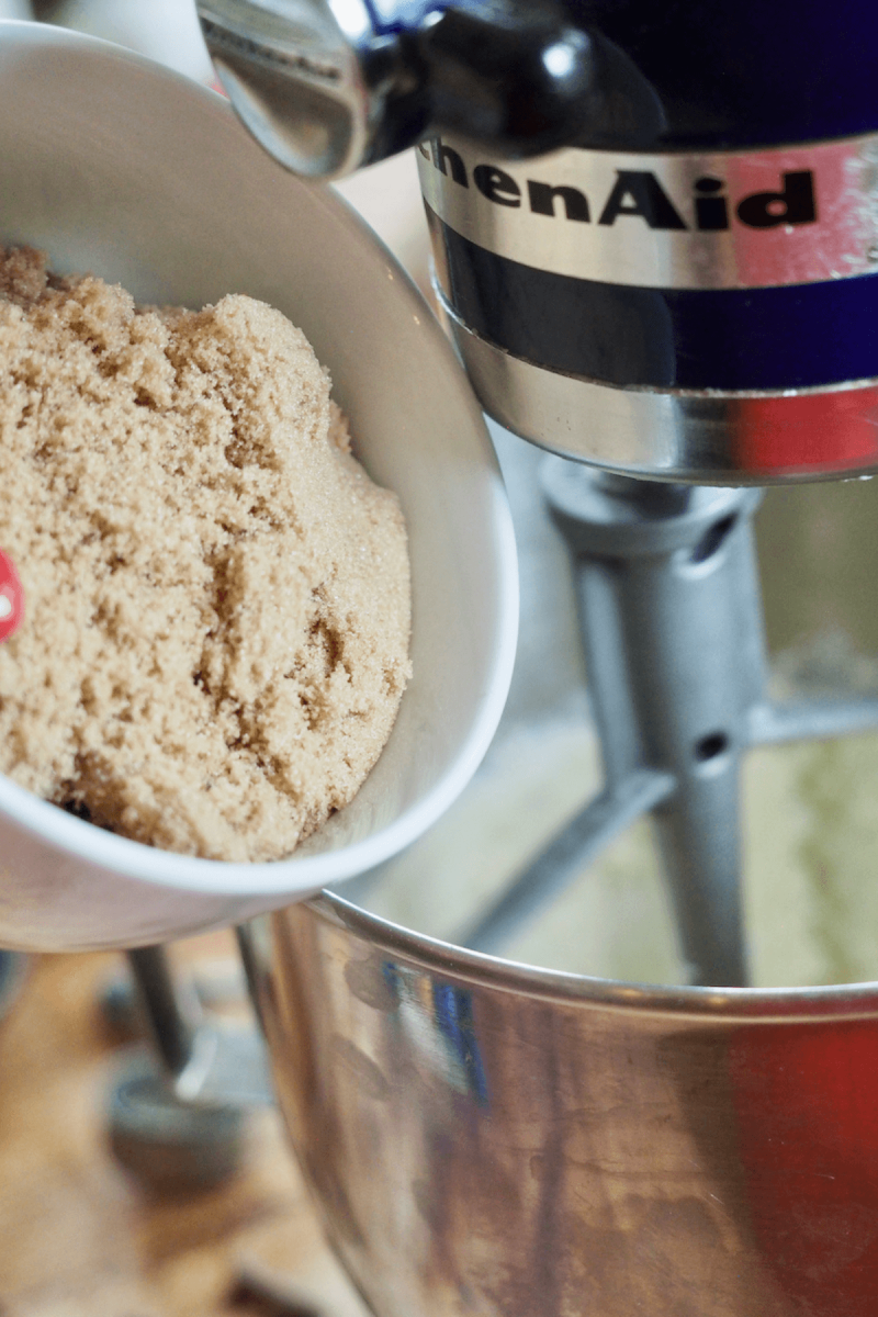 Adding packed light brown sugar into batter for crumbl cookies.