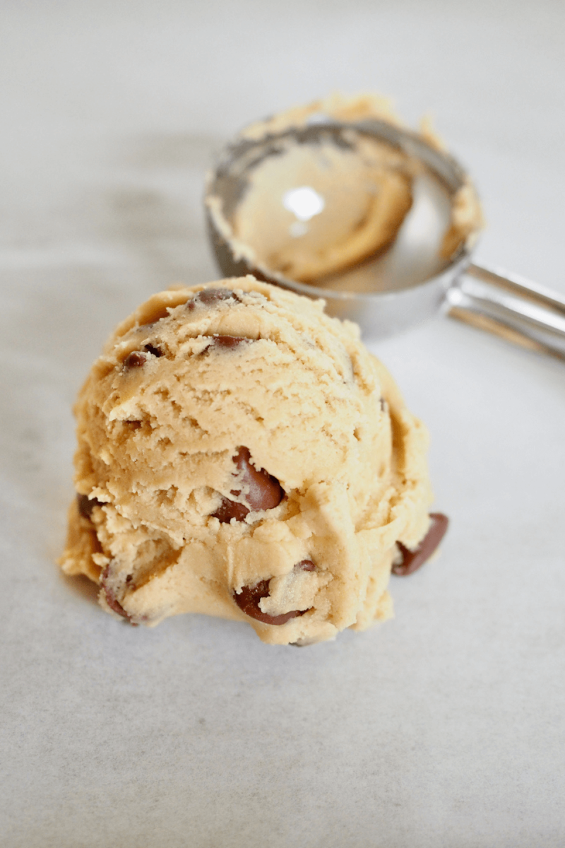 Giant cookie dough ball with scoop in background.